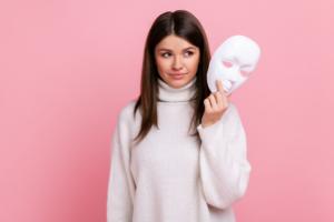Portrait of young beautiful adult female with dark hair looking away, holding in hands white mask.