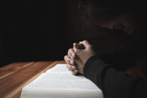 Silhouette of christian young woman praying with a cross and open the bible at sunrise, Christian Religion concept background.