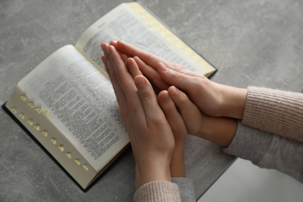 Boy and his godparent praying together at grey table, closeup
